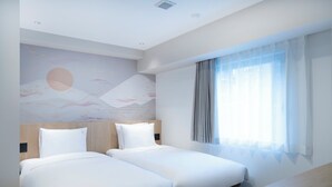 A hotel room with two single beds, a wooden headboard, a large window with sheer curtains, and a wall mural.