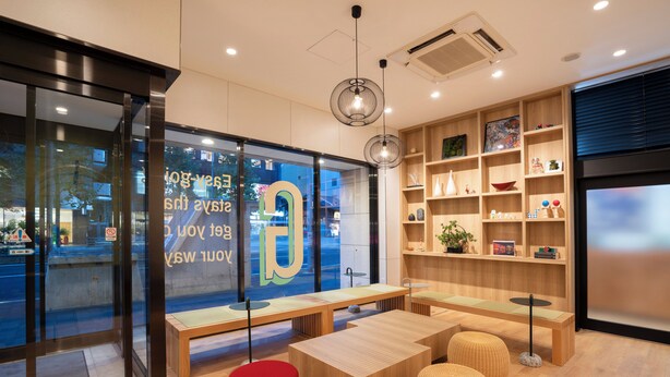 A modern interior with wooden furniture, a red stool, and a glass wall with a view of the street.