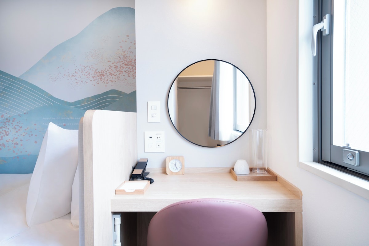 Una habitación de hotel con una cama, un escritorio con espejo, un reloj y una ventana.