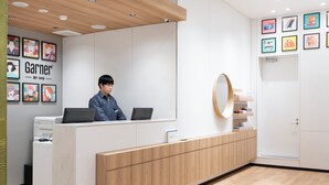 A modern reception desk with a man seated behind it, a wooden panel design, and framed artwork on the walls.