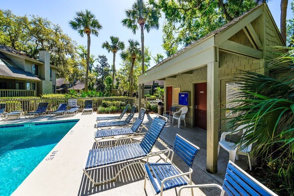 A poolside area with lounge chairs, a pool, and a building with a sign reading "POOL AREA". - Sunset Rentals | Fazio 34 (Hilton Head)