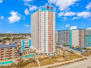 A high-rise hotel with multiple floors, a swimming pool, and a beach area.