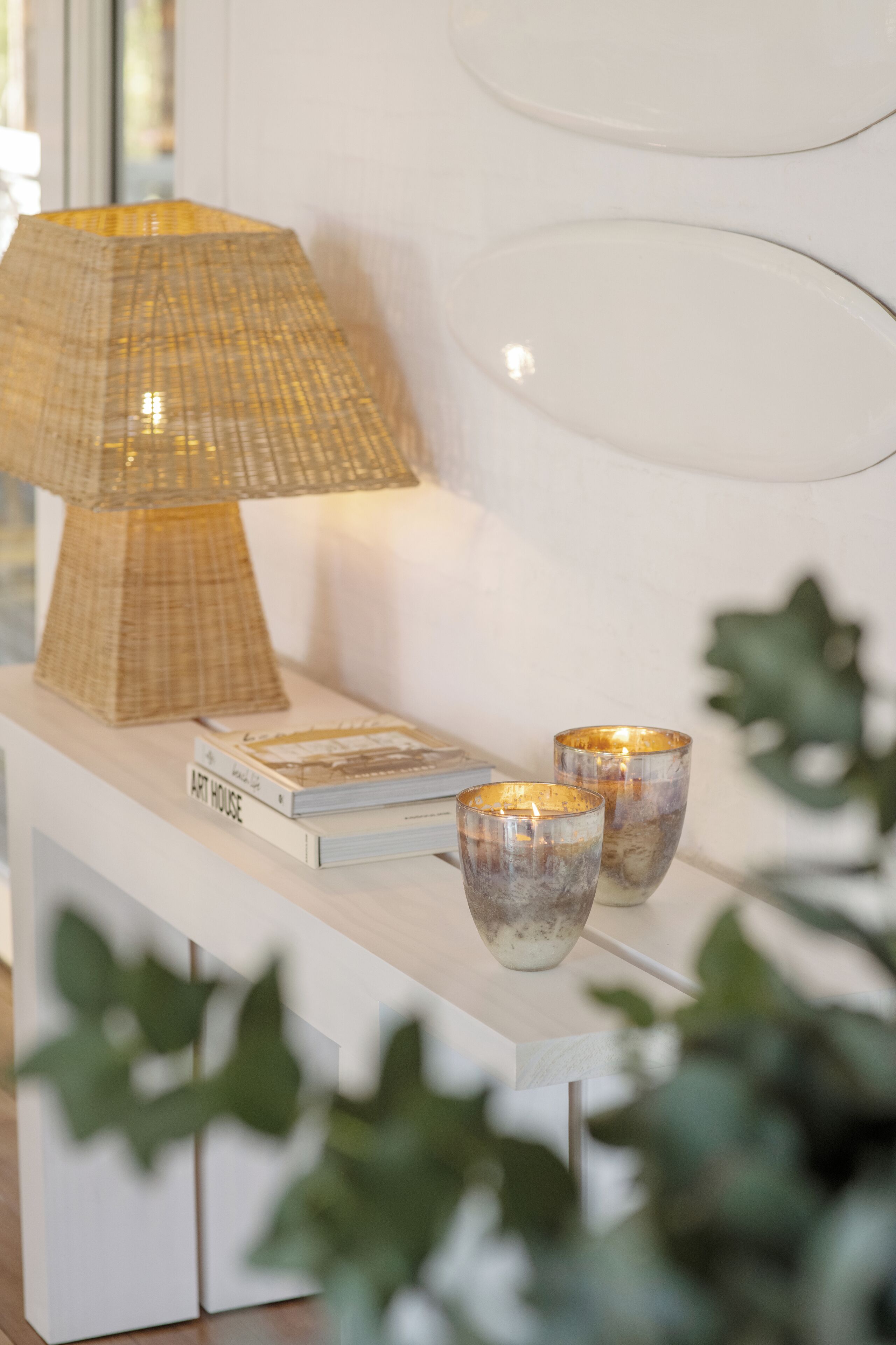 A white console table with a lamp, two books, and two candle holders.