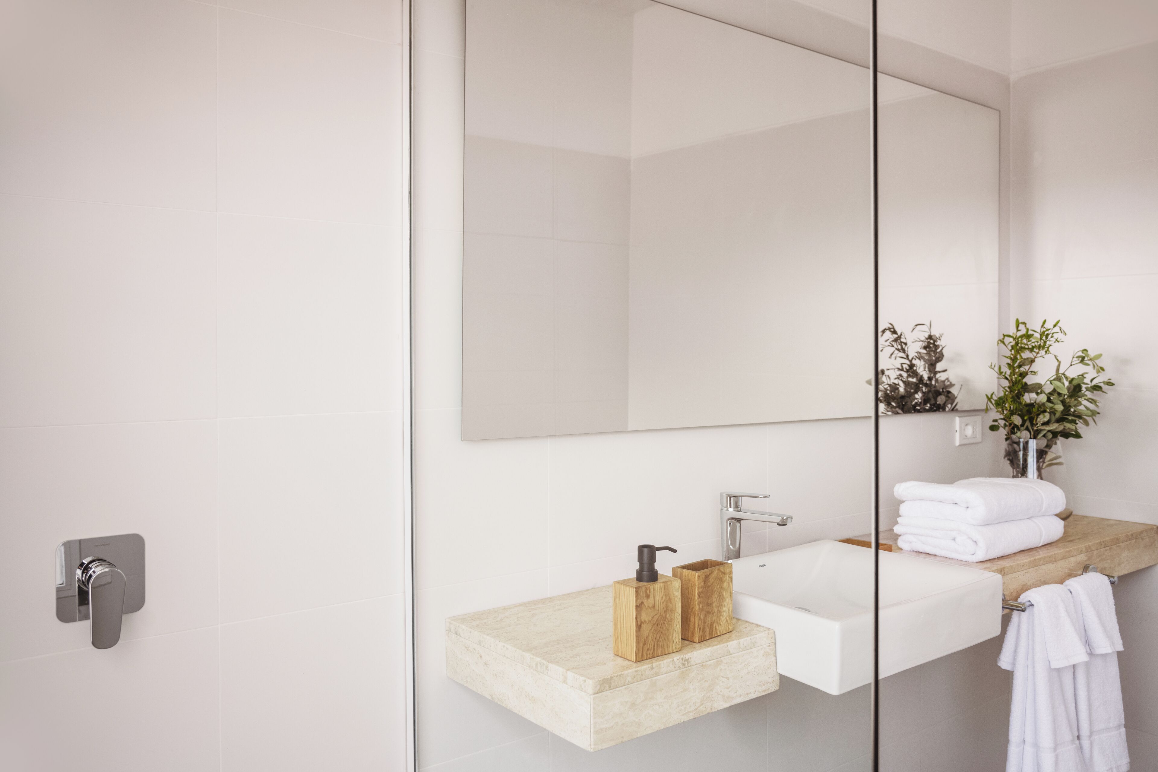 A modern bathroom with a glass shower enclosure, a white sink with a wooden vanity, and a large mirror.