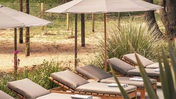 A poolside area with lounge chairs and umbrellas, surrounded by trees and greenery.