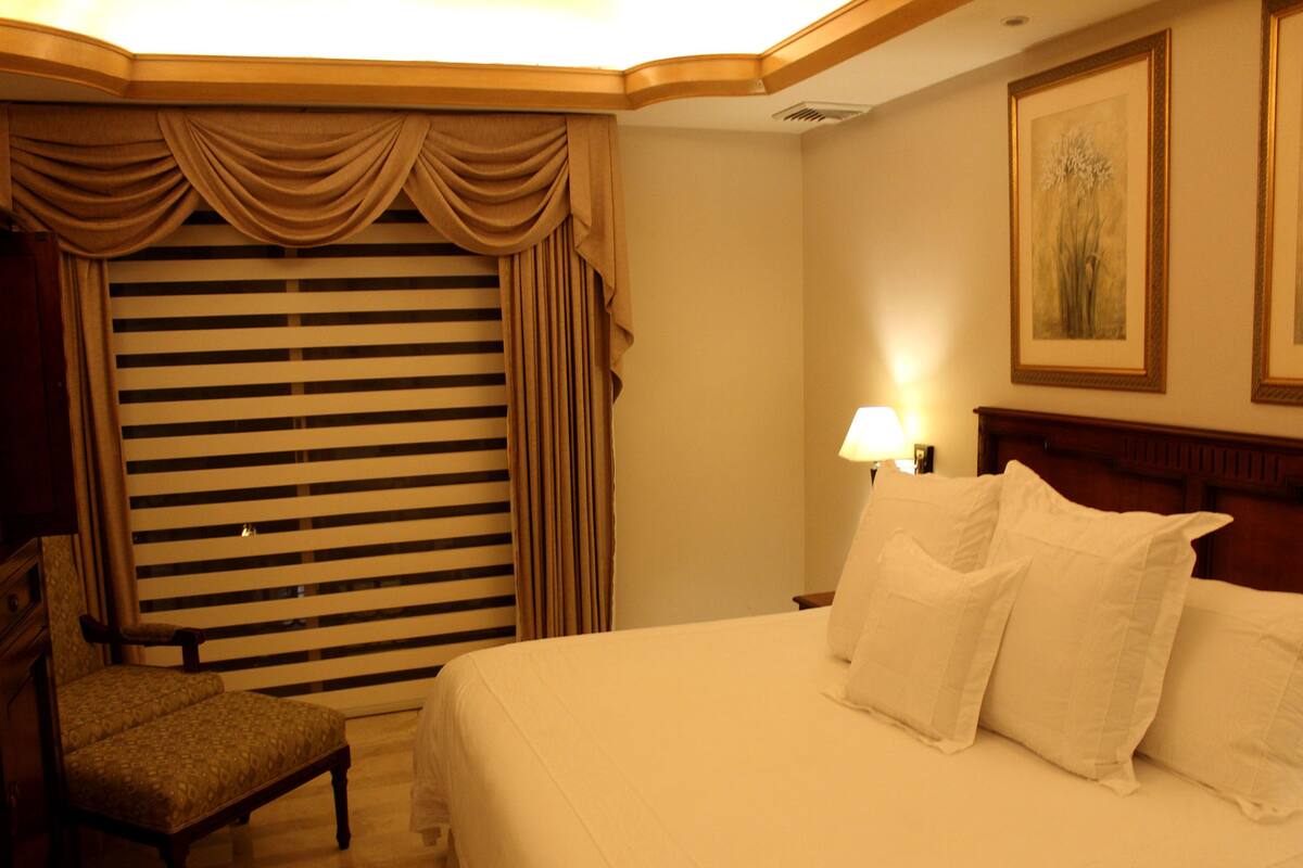 Una habitación de hotel con una cama, una silla, una lámpara y un cuadro en la pared.