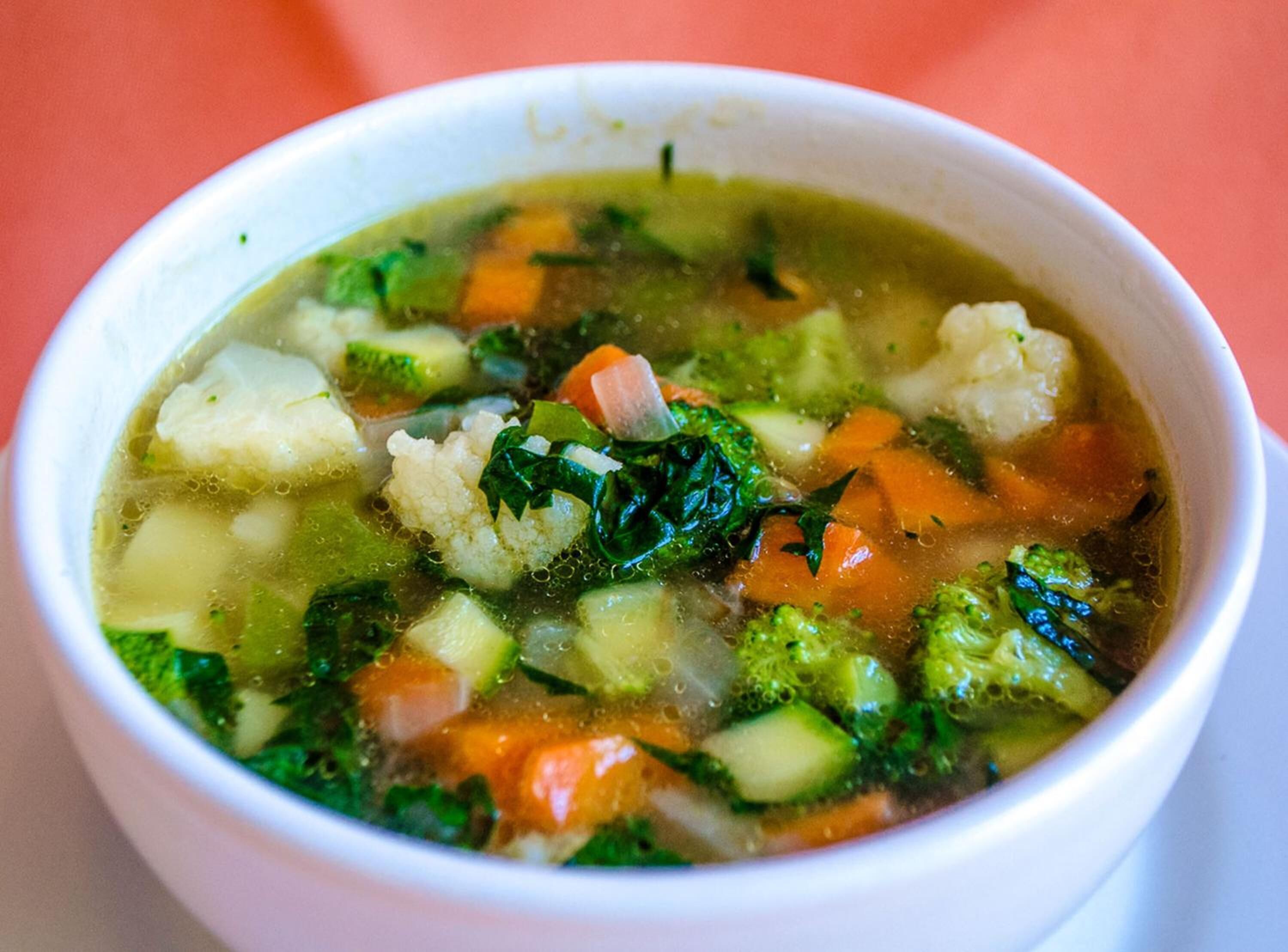 Un bol de soupe aux légumes contenant des ingrédients clairement visibles, comme des carottes, des brocolis et des légumes verts à feuilles.