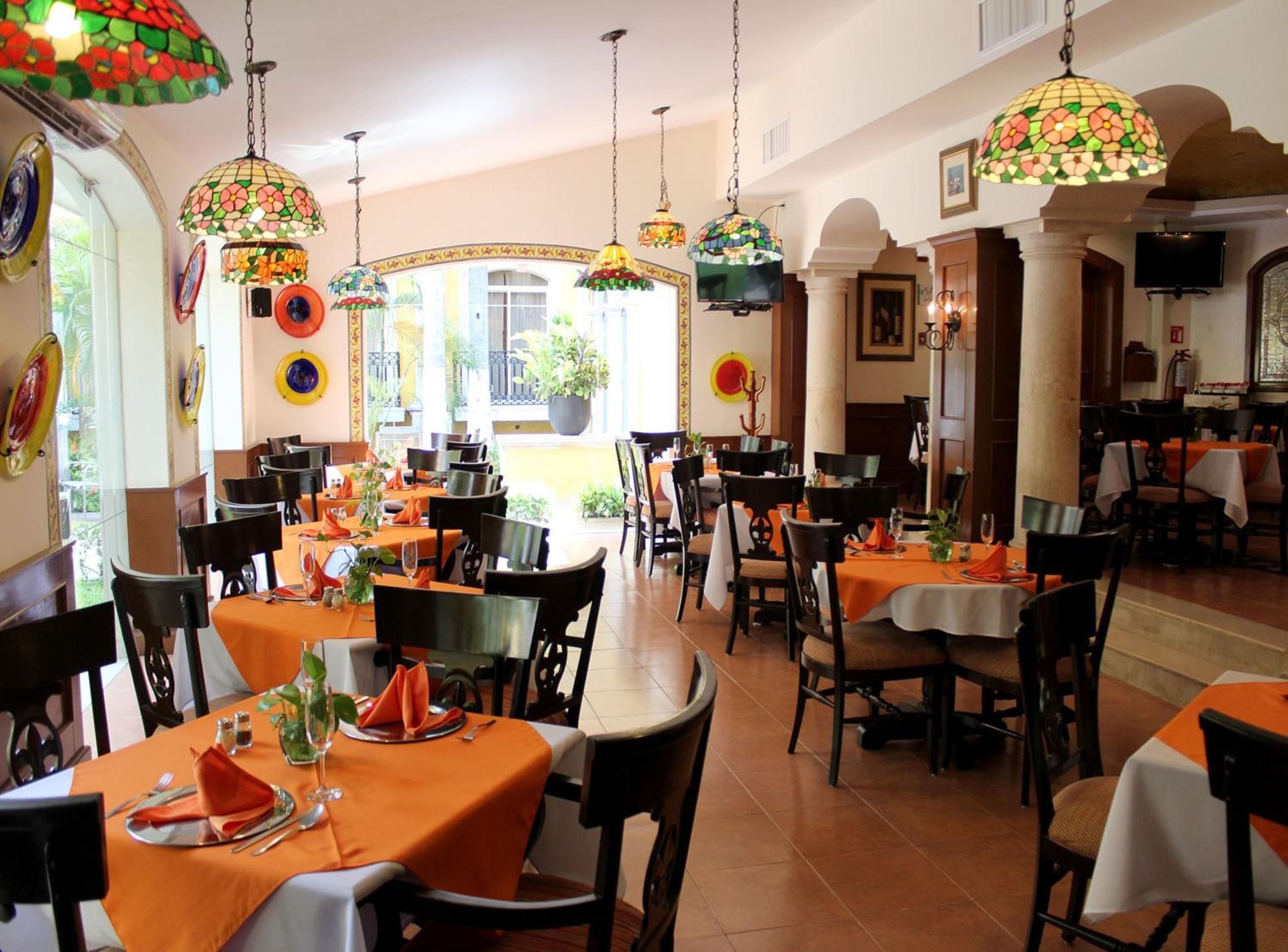 Un restaurante con varias mesas, manteles naranjas y lámparas colgantes de colores.