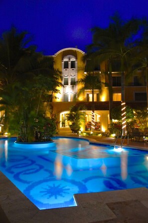 Un hotel con piscina, palmeras y una fachada iluminada.
