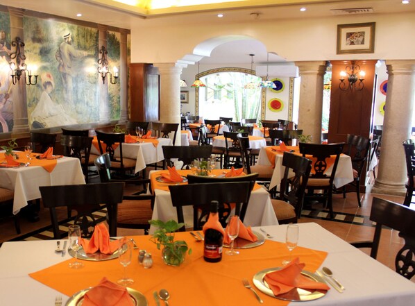 Un restaurante con varias mesas dispuestas para comer, con manteles anaranjados y vajilla blanca.