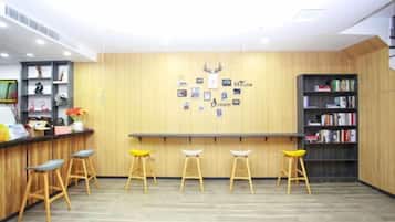 Un área de recepción con mostrador de madera, tres taburetes, una estantería y una pared con cuadros enmarcados y la inscripción “House Dream”.