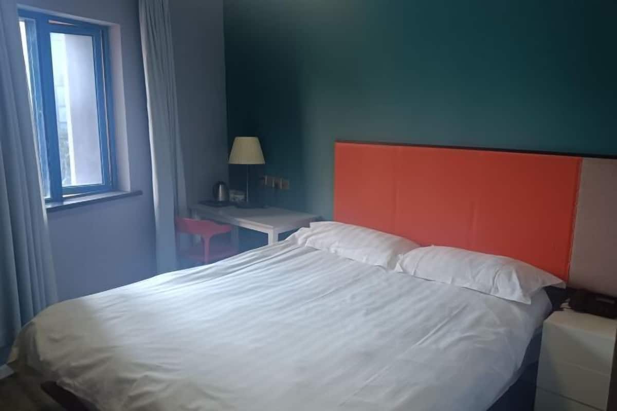 A hotel room with a bed, a desk, a chair, and a window with curtains.