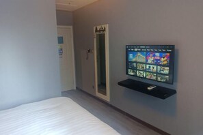 A hotel room with a bed, a TV mounted on the wall displaying various channels, and a door with a mirror. - OK Boutique Hotel (Shanghai)