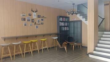 A hotel lobby with a wooden wall, a reception desk, a staircase, and a bookshelf.