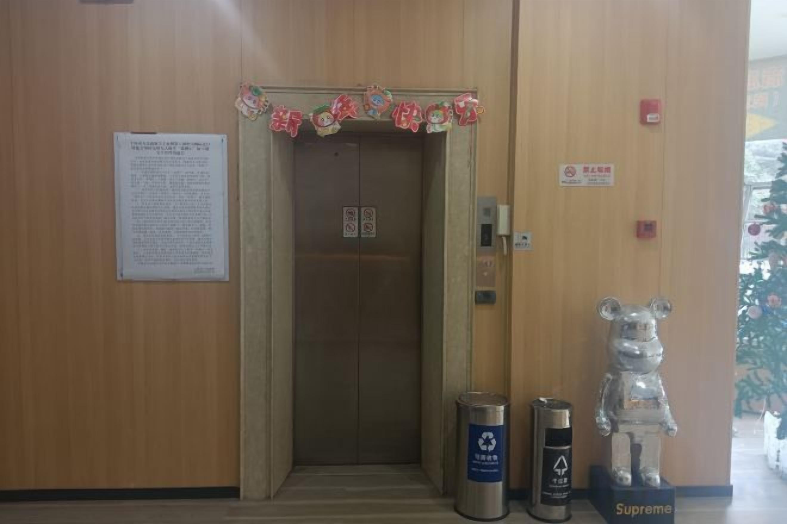 An elevator with a wooden wall, a trash bin, and a bear statue.