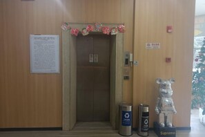 An elevator with a wooden wall, a trash bin, and a bear statue.