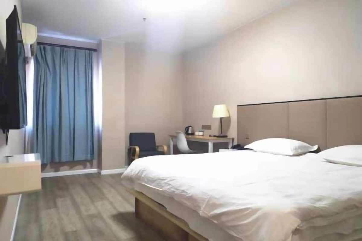 A hotel room with a bed, a desk, a chair, a lamp, and a TV.