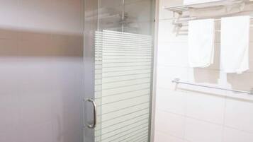 A modern bathroom with a glass shower enclosure, a glass door, and a towel rack with folded towels.