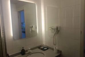 A bathroom with a large mirror, two hair dryers mounted on the wall, a sink, a small tray with toiletries, and a toilet paper roll. - OK Boutique Hotel (Shanghai)