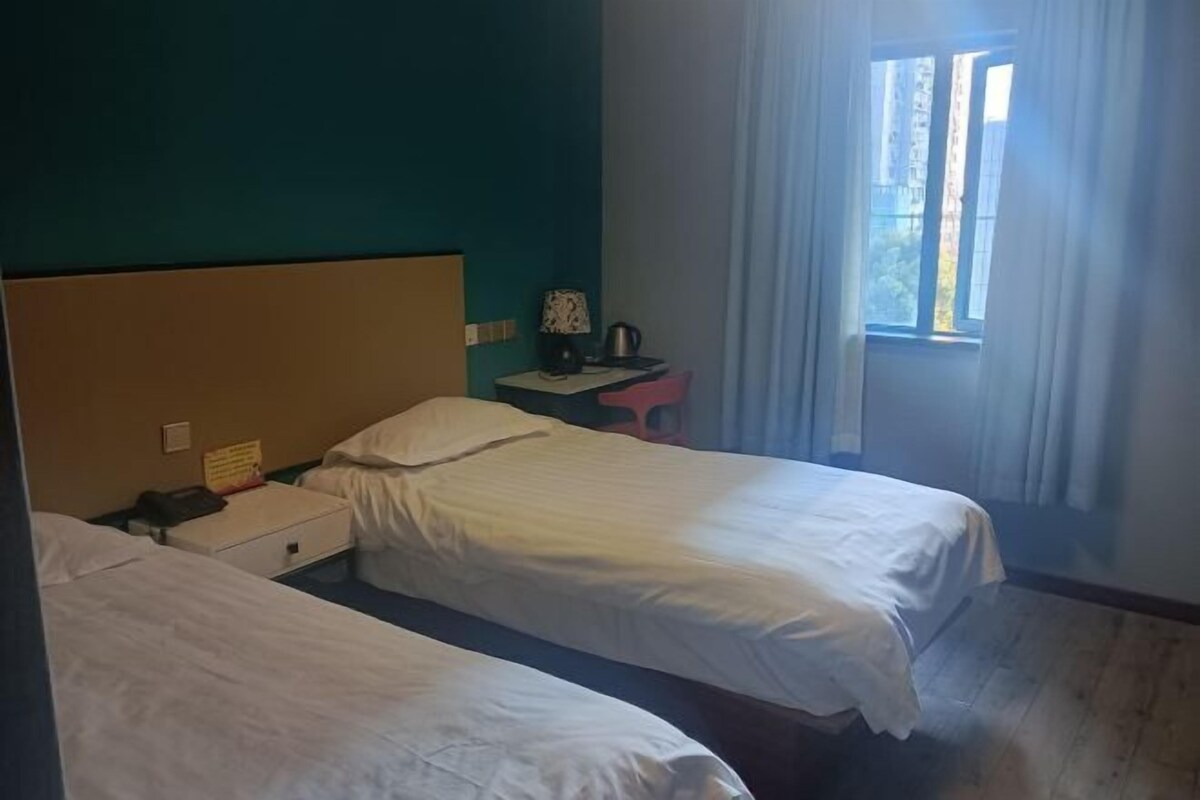 A room with two beds, a small table with a lamp, and a window with curtains.