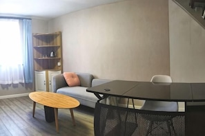 Una sala de estar moderna con un sofá, una mesa redonda de madera, una mesa de comedor negra y una estantería.