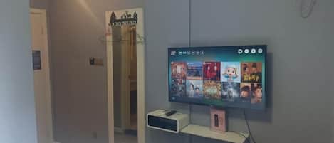 A bedroom with a TV mounted on the wall, a bedside table, and a mirror.