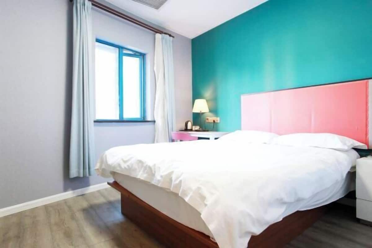 A bedroom with a bed, a nightstand, a lamp, and a window with curtains.