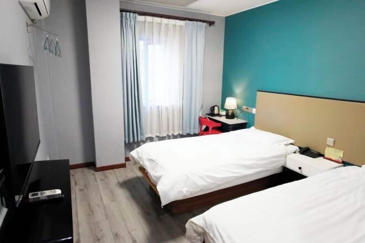 A hotel room with two beds, a TV, a desk, and a window with curtains.