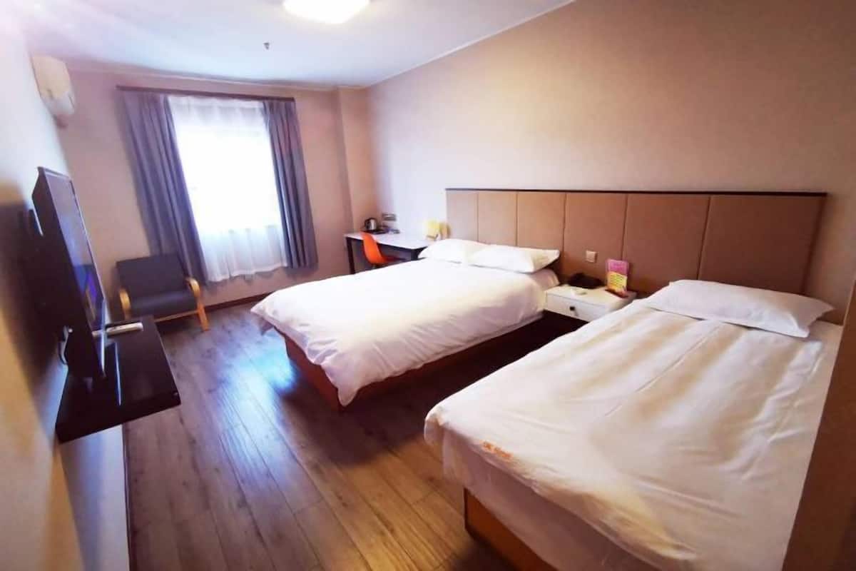 A hotel room with two beds, a desk, a chair, a TV, and a window with curtains.