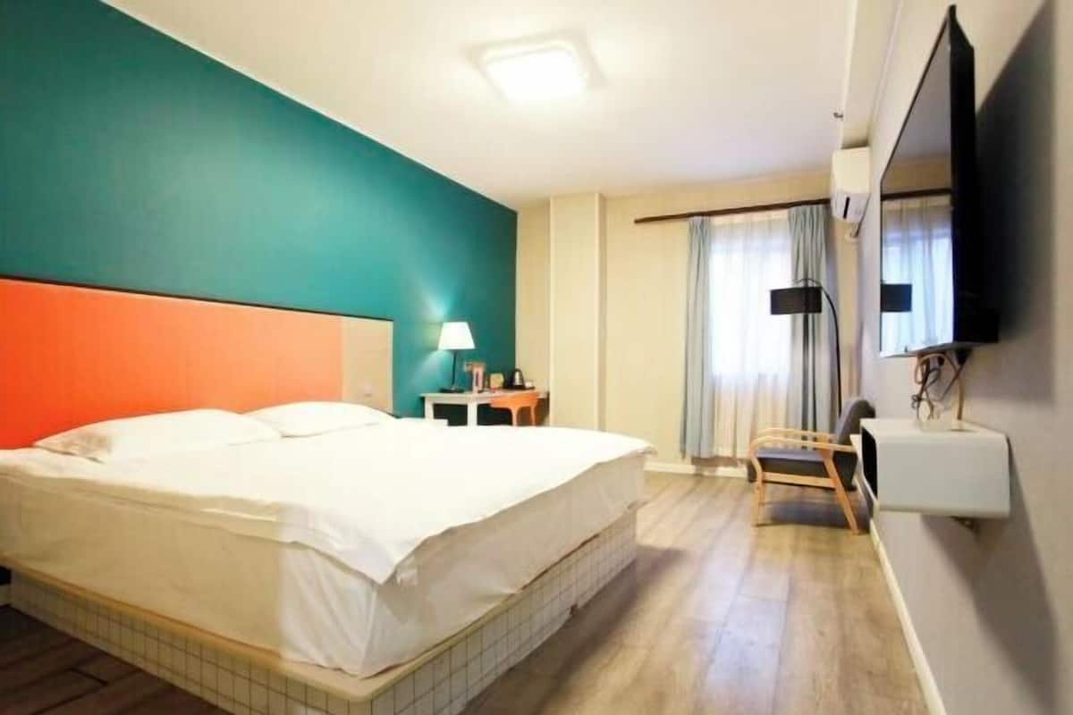 A hotel room with a bed, a desk, a chair, a TV, and a window with curtains.