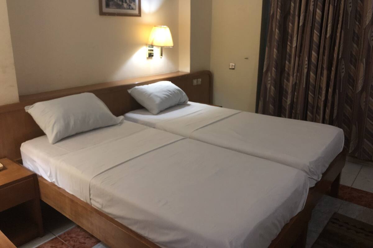 A double bed with white linens, a nightstand, a wall-mounted lamp, and a framed picture on the wall.