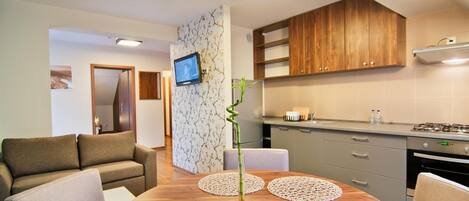 A modern living room with a round wooden table, two sofas, and a TV mounted on a wall with a tree pattern wallpaper.