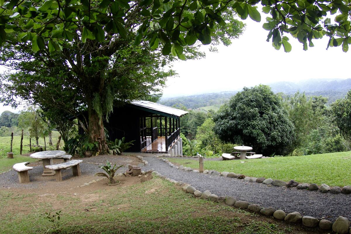 A covered outdoor seating area with stone benches and a table, surrounded by a gravel path and a stone border.
