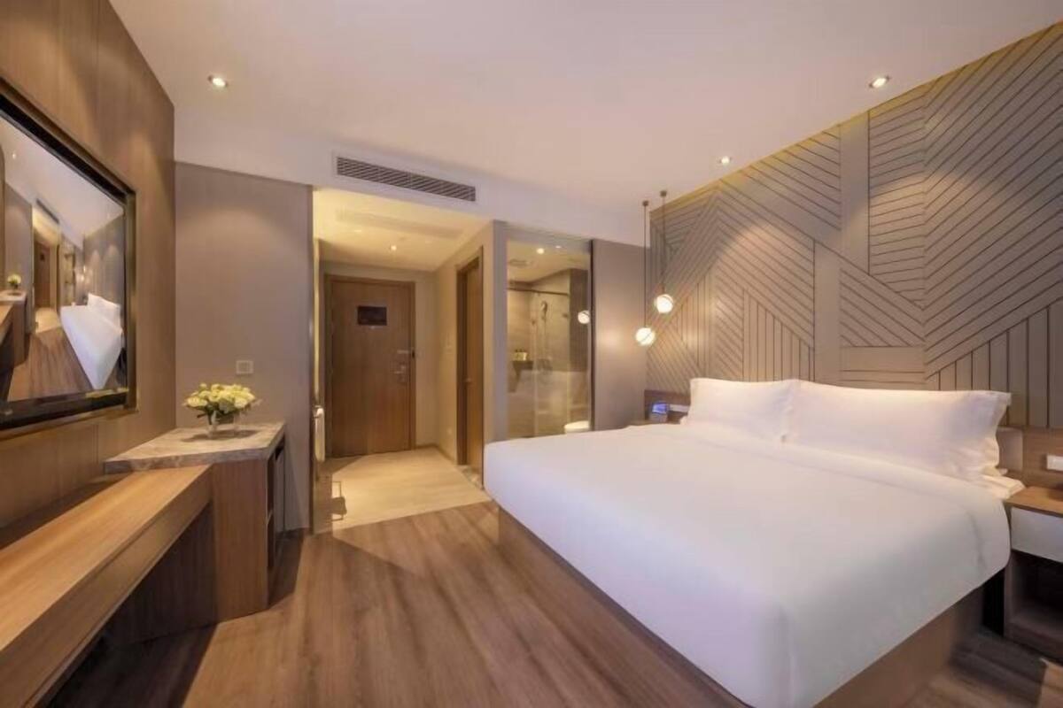 Une chambre d’hôtel moderne avec un grand lit, un bureau en bois, un miroir et un téléviseur fixé au mur.
