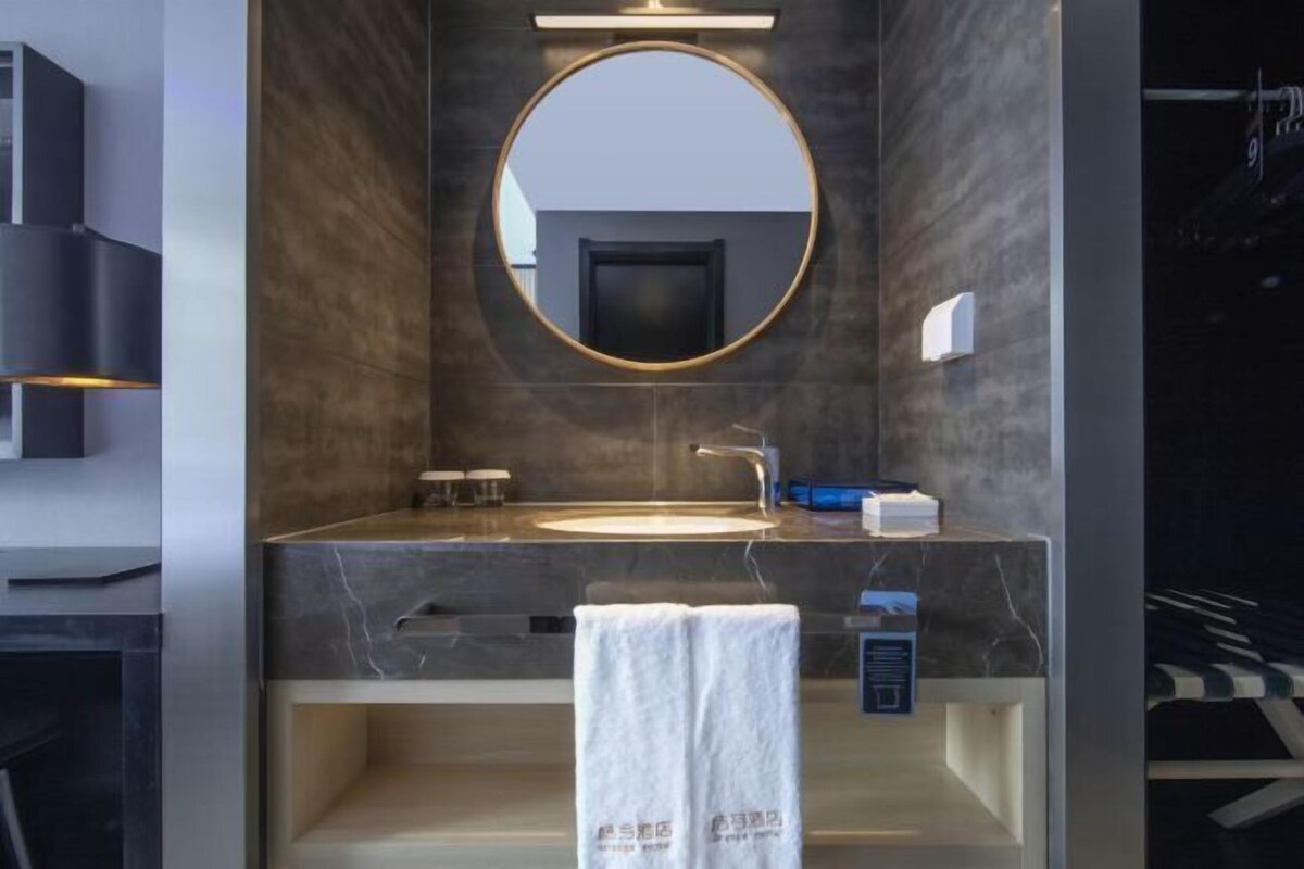 A modern bathroom with a round mirror, a sink, and a towel hanging on a rack.