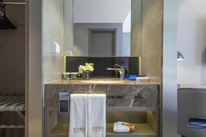A modern bathroom with a marble countertop, a sink, a mirror, a towel rack, and a shelf with toiletries. - Orange Hotel (Shanghai Jiaotong University, Jiangchuan Road Metro Station) (Shanghai)