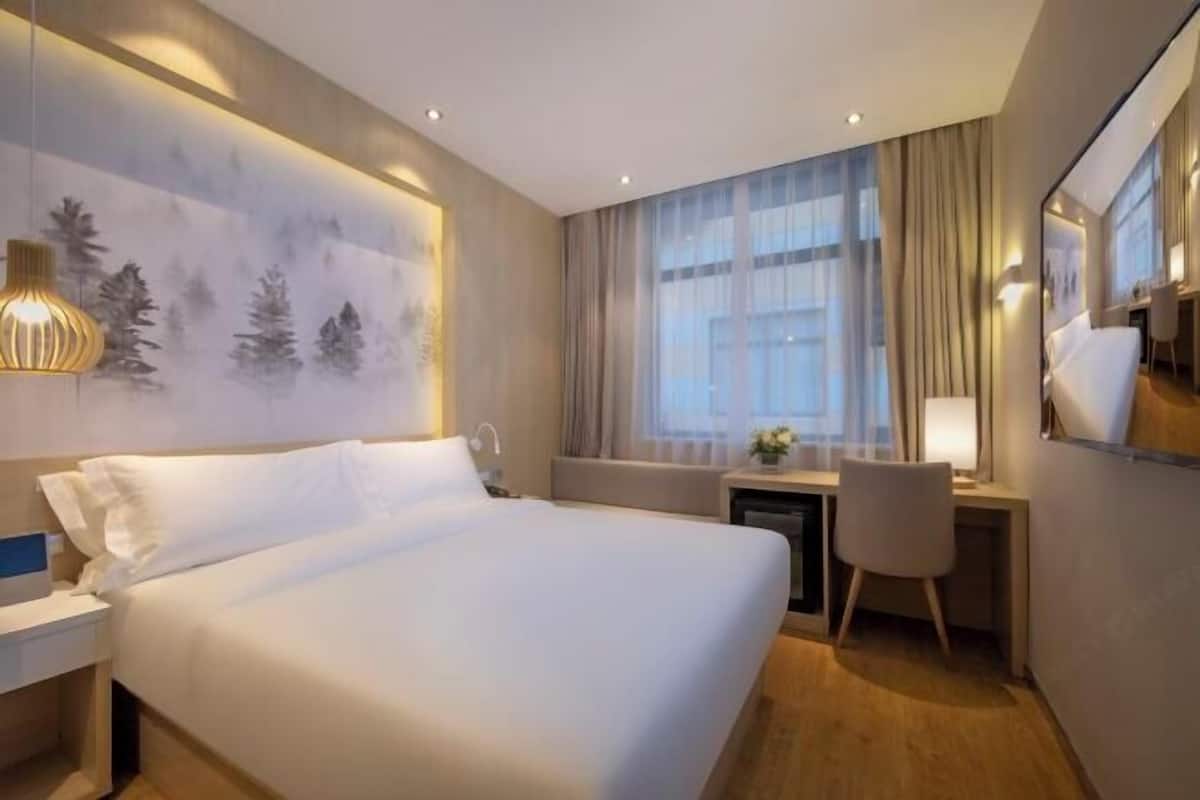 Une chambre d’hôtel avec un grand lit, un bureau, une chaise et une grande fenêtre avec des rideaux.