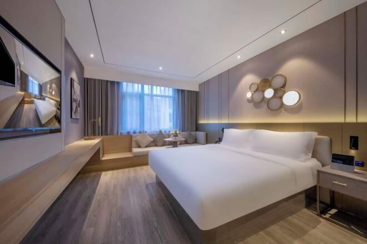 Une chambre d’hôtel moderne dotée d’un grand lit, d’un coin salon, d’une télévision et d’un luminaire fixé au mur.