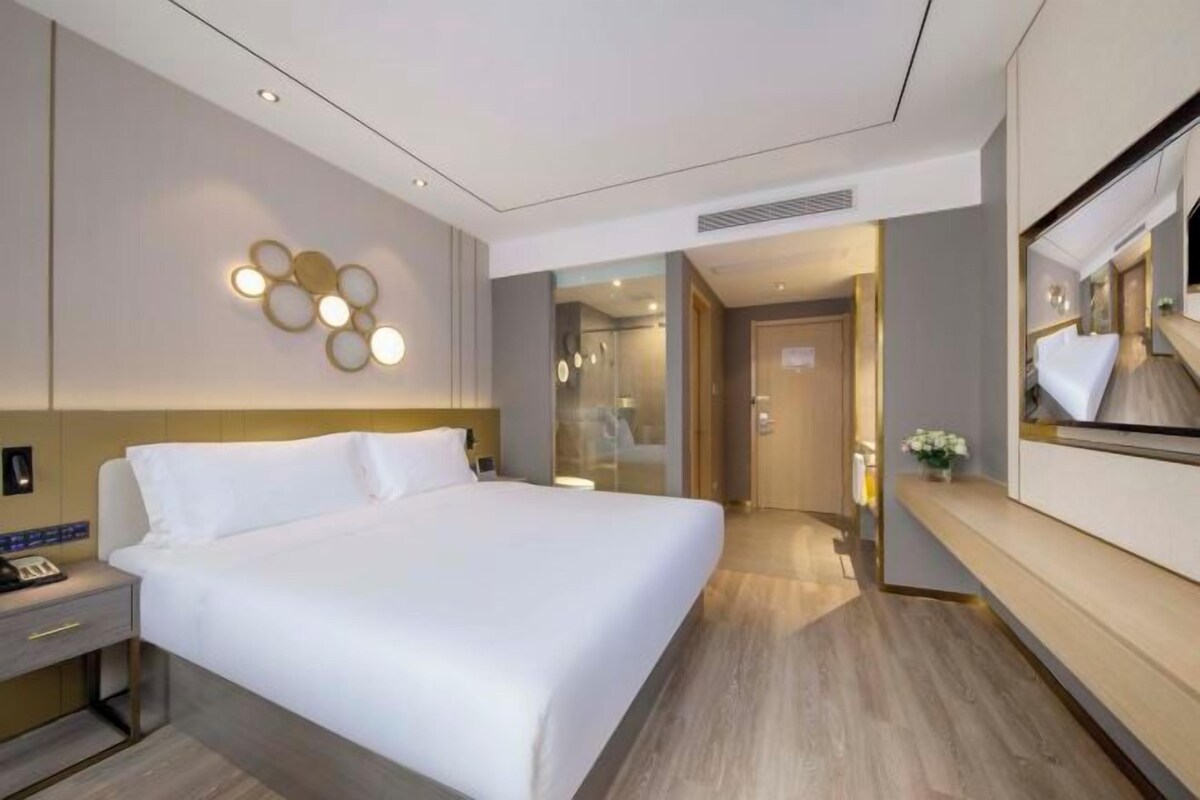 A modern hotel room with a large bed, bedside table, and a mirror.