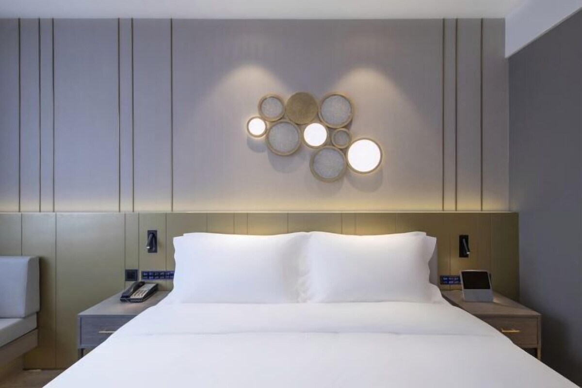 A modern hotel room with a large bed, bedside tables, a wall-mounted light fixture, and a telephone.