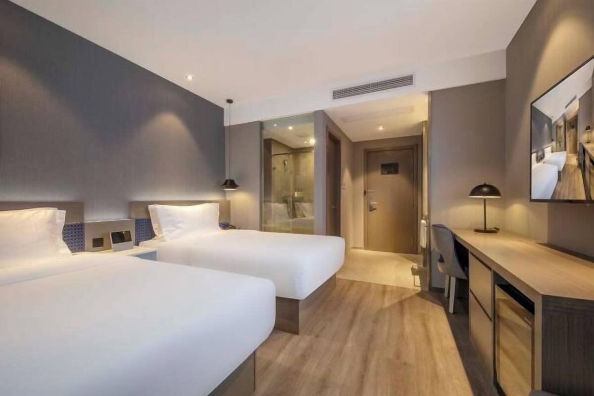 Une chambre d’hôtel avec deux lits, un bureau, un miroir et un espace douche.