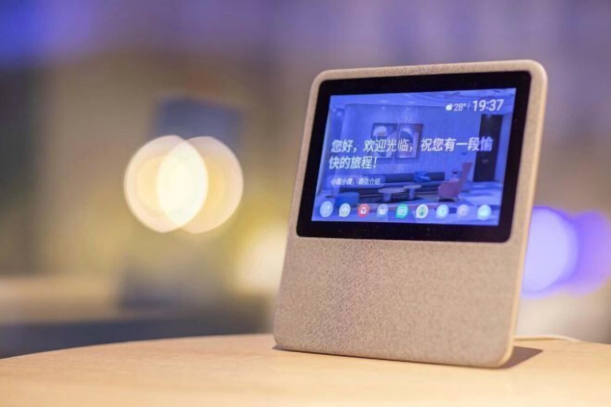 A tablet on a stand displaying a room with a bed, a chair, and a table.