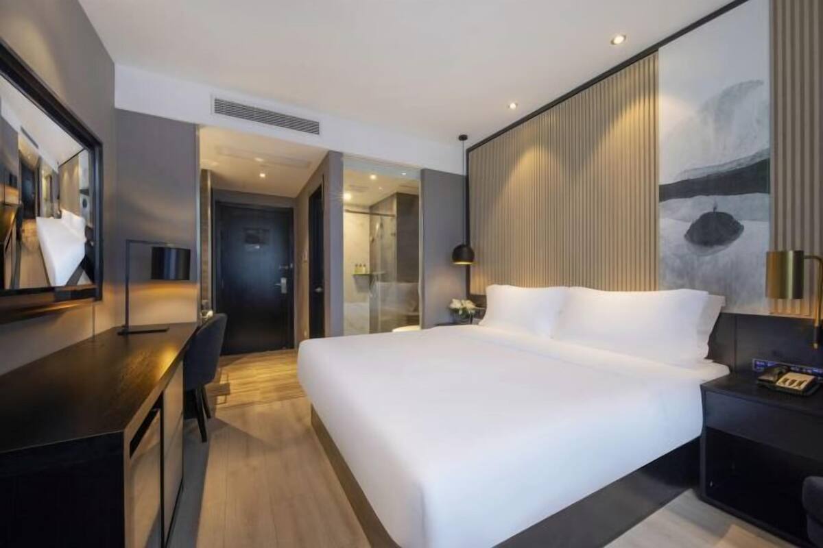 Une chambre d’hôtel moderne équipée d’un grand lit, d’un bureau, d’une chaise, d’une table de chevet et d’un miroir.