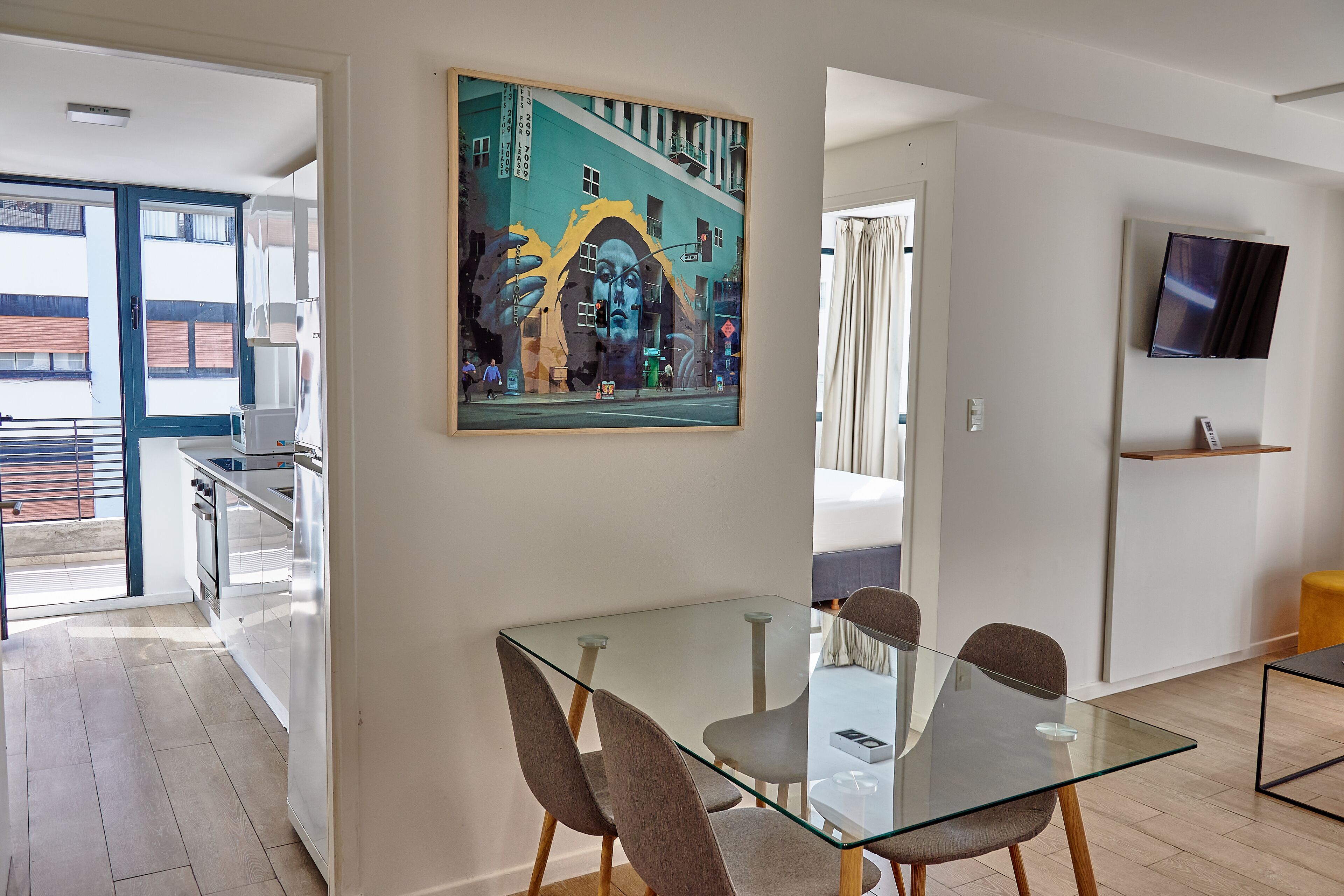 Eine moderne Küche mit einem Glastisch, einem Bild an der Wand und einem an der Wand befestigten Fernseher.