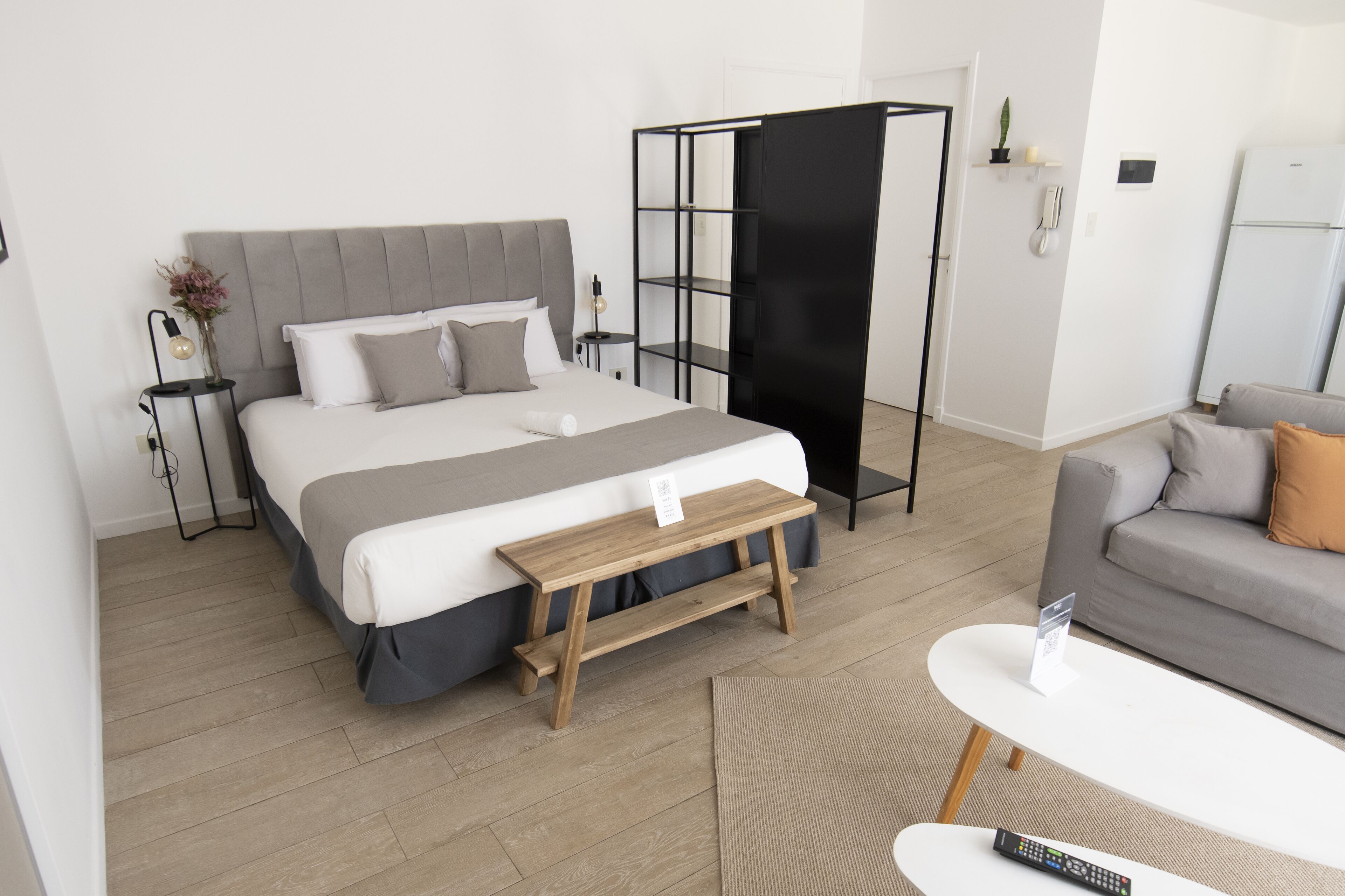Ein modernes Schlafzimmer mit Bett, Nachttischen, einer kleinen Holzbank, einem Sofa und einem Couchtisch.