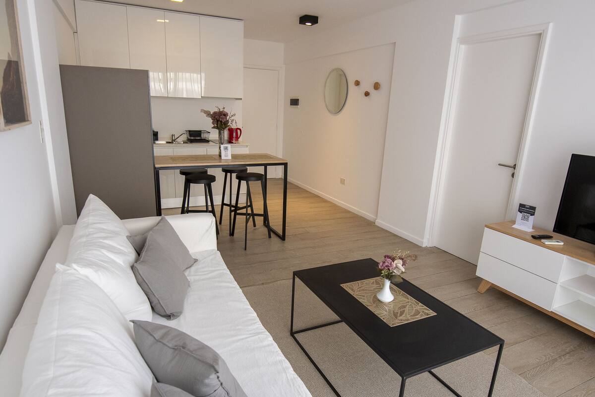 A modern living room with a white sofa, black coffee table, and a TV on a wooden stand.