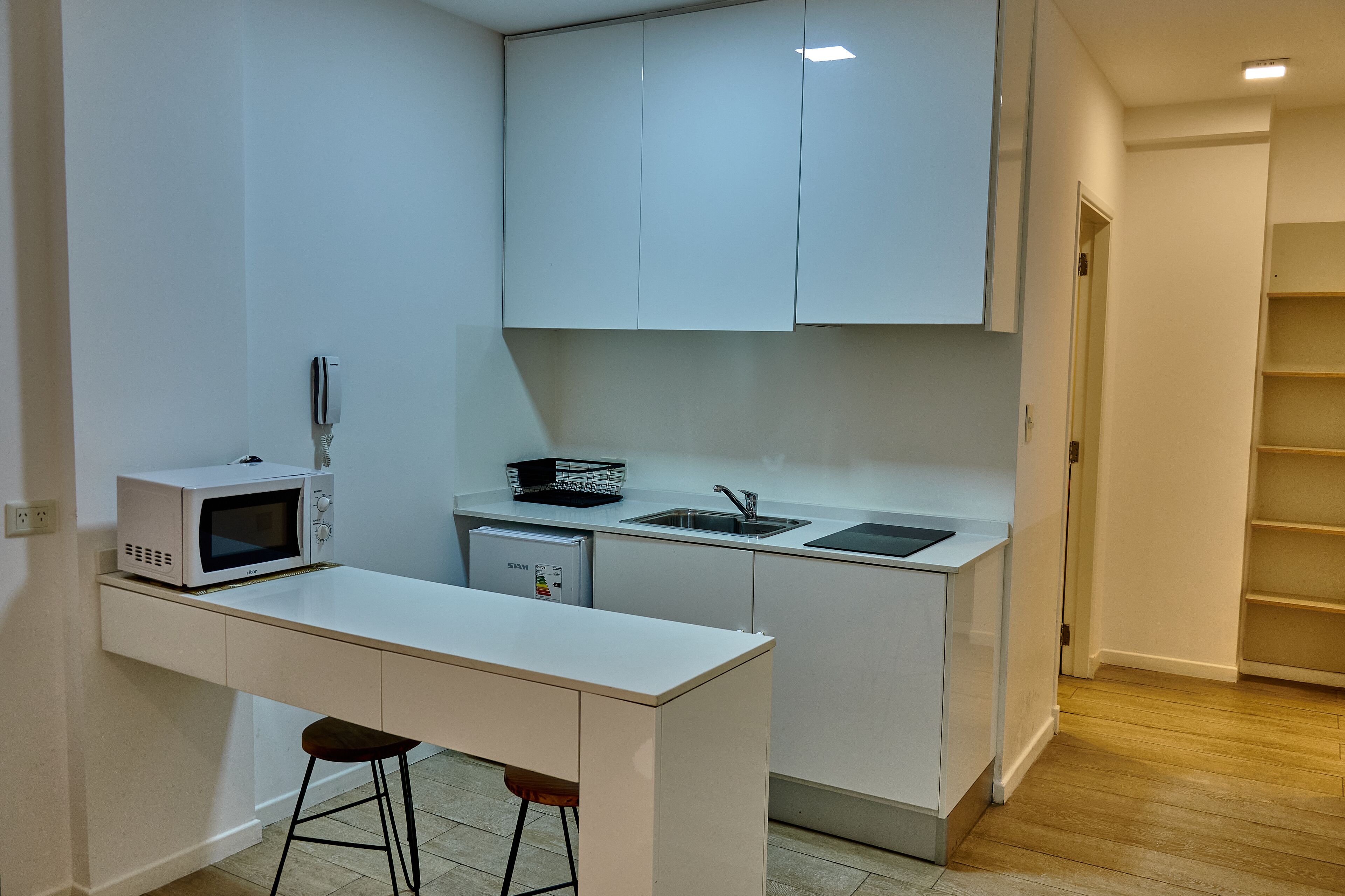 Una cucina compatta con mobili bianchi, un forno a microonde, un piccolo frigorifero e un lavello.