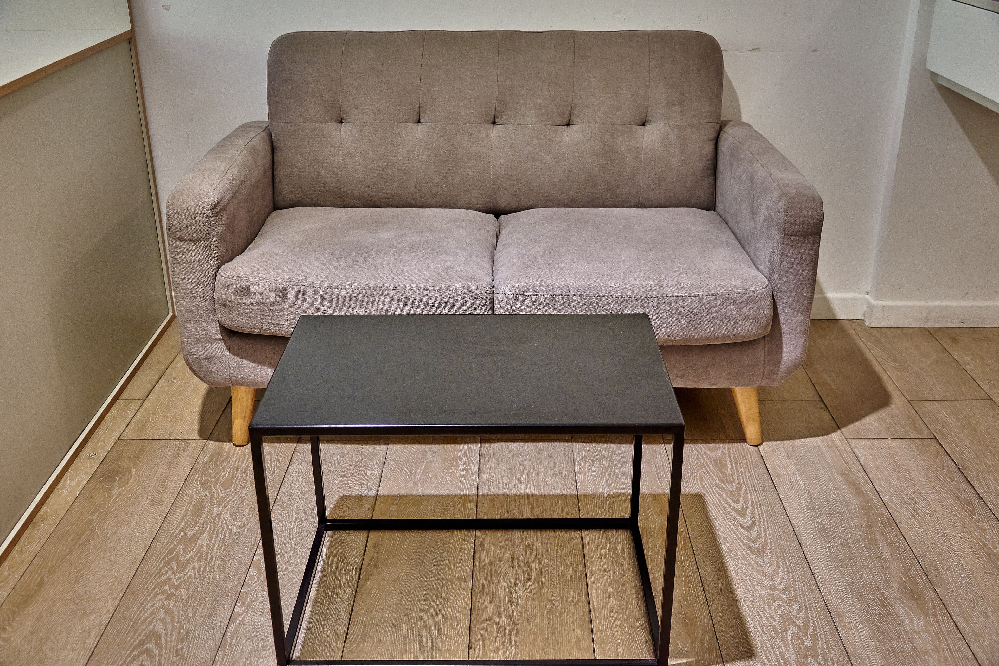 A beige sofa with wooden legs and a black metal table in front of it.