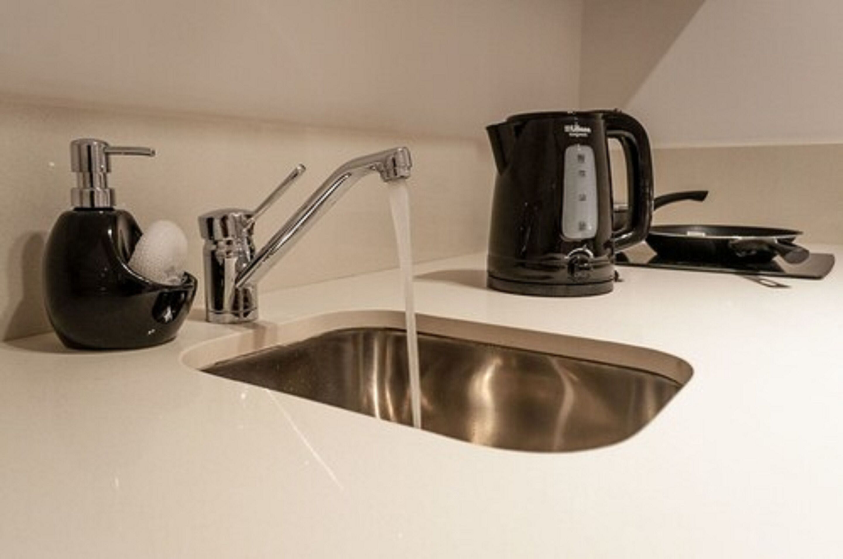 Un évier de cuisine avec de l’eau courante, un distributeur de savon et une machine à café.