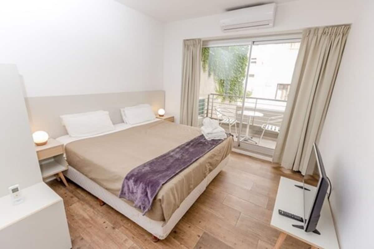 A hotel room with a bed, bedside tables, a TV, and a balcony with a view.